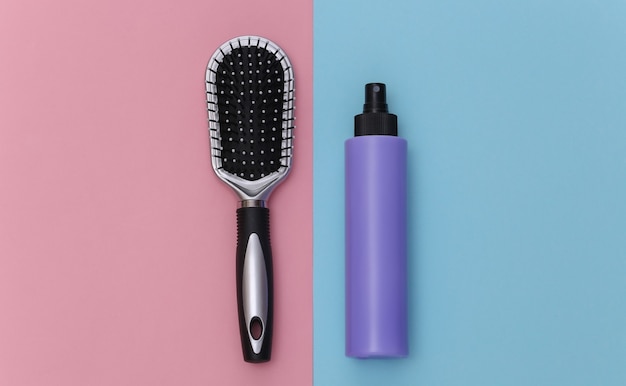 Bottle of hairspray, hair brush on pink blue pastel background. Top view