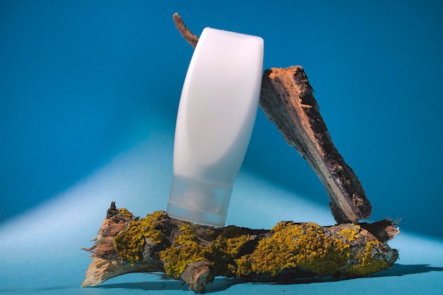 A bottle of hand cream sits on a branch with a blue background.