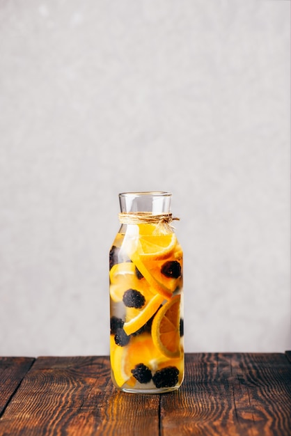 Бутылка настоянной воды с нарезанным сырым апельсином и свежей ежевикой.
