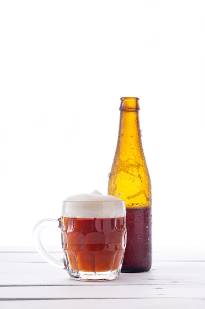 Bottle and jug of beer on white wooden base. Vertical format.