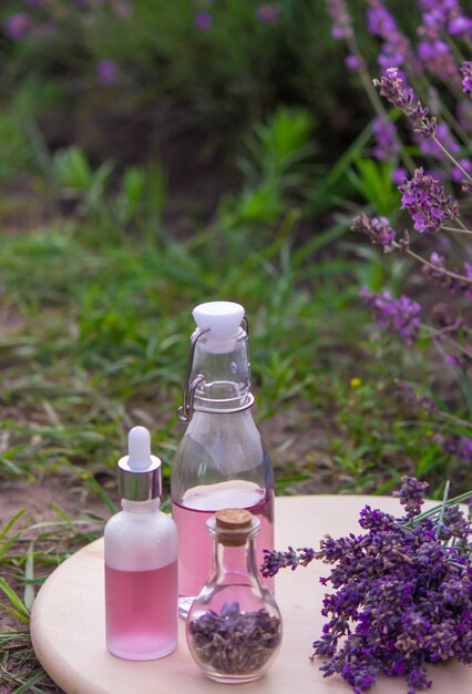 A bottle of lavender essential oil on a wooden table and a field of flowers background