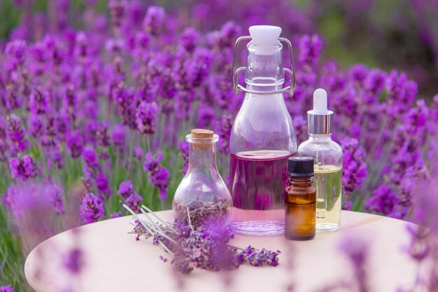 A bottle of lavender essential oil on a wooden table and a field of flowers background