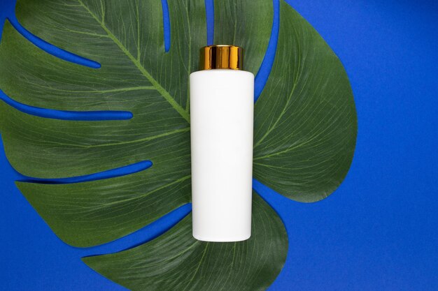 Bottle for liquid, cream, gel, lotion. Cosmetic Bottle on blue with tropical leaf. Flat lay