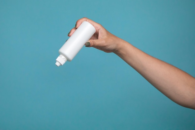 A bottle of liquid for lenses in woman hand on a blue background. Mock up of liquid for lenses