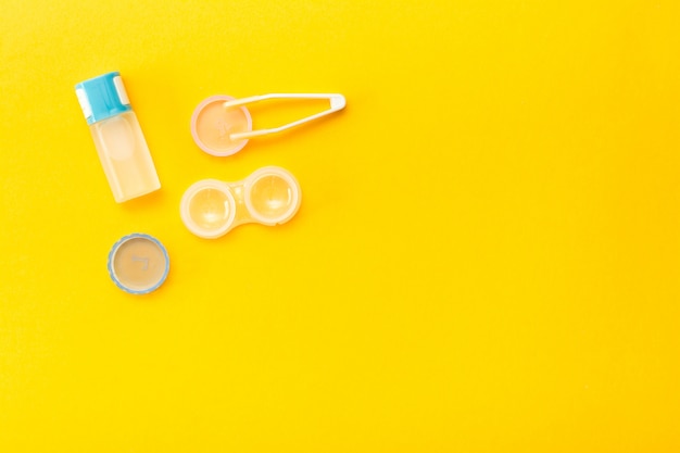 a bottle of liquid, open container and tweezers on a yellow background. 