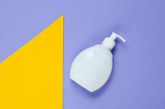 Bottle of liquid soap on on colored paper with geometric shapes