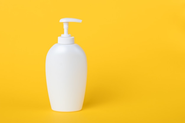 Bottle of liquid soap, white plastic flacon with dispenser on a yellow wall. Copy space, empty place for text. Pump lotion. Shower gel for body. Personal hygiene concept.