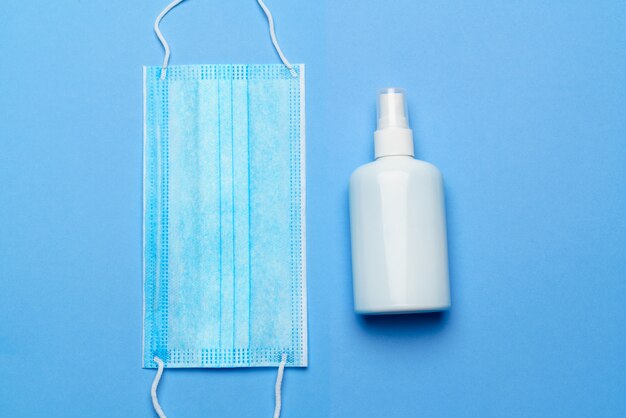 Bottiglia di lozione, disinfettante o sapone liquido e maschera protettiva su sfondo blu - layout piatto