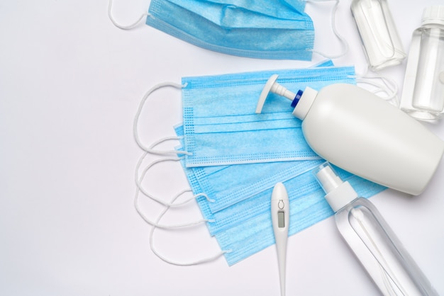 Bottle of lotion, sanitizer or liquid soap, thermometer and medical protective mask over light grey wall.