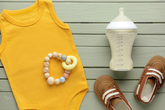 Bottle of milk for baby with clothes on color background