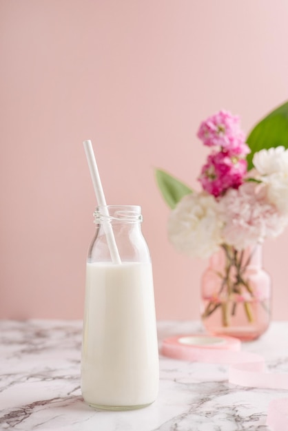 Bottiglia di latte e fiori sulla tavola di marmo sopra lo spazio rosa della copia del fondo