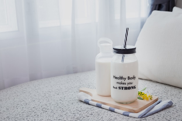 bottle of milk and glass of milk on bed in living room with white curtain windows.