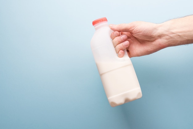 Bottle of milk in a man's hand on a blue background.