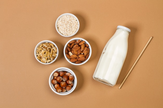 A bottle of milk with nuts in white bowls on a brown background in a top view