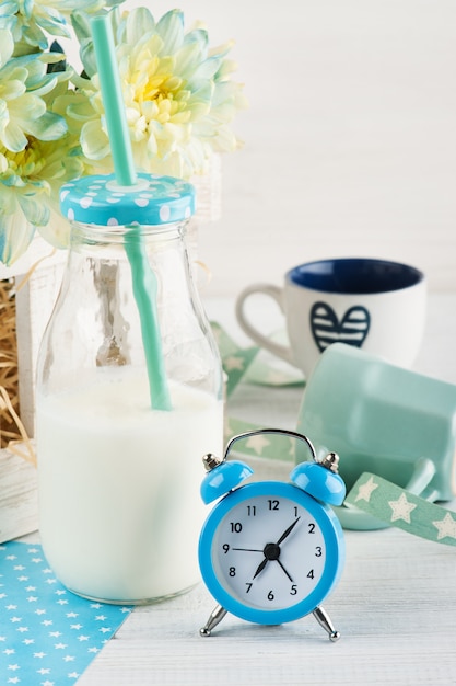 Bottle of milk with straw and blue alarm clock