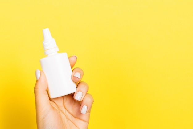 A bottle of nasal spray in a female hand at yellow