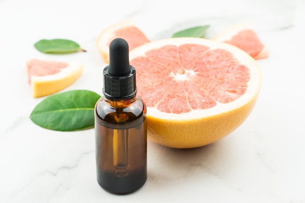 A bottle of natural grapefruit oil on a white table with grapefruit fruits. the concept of facial care. prevention of age-related skin changes.