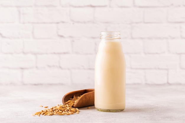 A bottle of oat milk and oats on a light background.