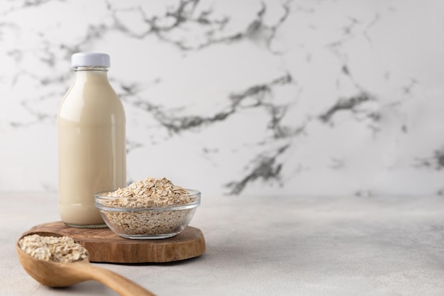 A bottle of oat milk on a wooden board with an ingredient in a bowl on a light background