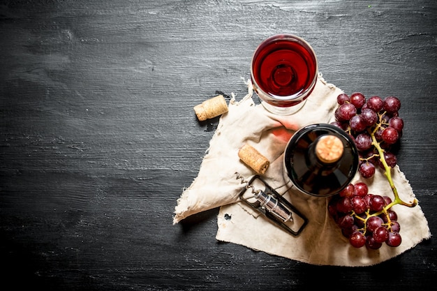 Фото Бутылка красного вина с гроздью винограда на старой ткани на черном деревянном столе.