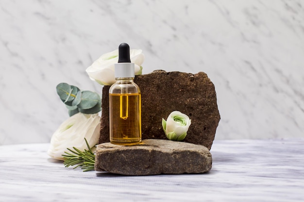 Bottle of oil for hair repair Homemade skin or hair care and beauty treatment natural cosmetics placed on stones Composition of bottle with pipette small green flowers on white background
