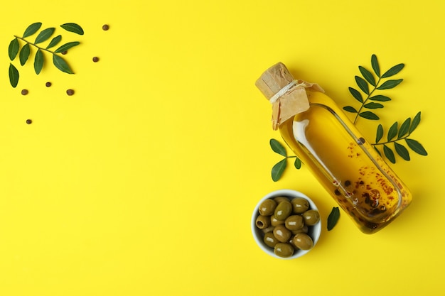 Bottle of oil, olives, twigs and pepper on yellow surface