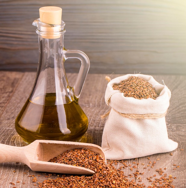 Bottle of oil sesame seeds in sack on wooden table on soft sunlight