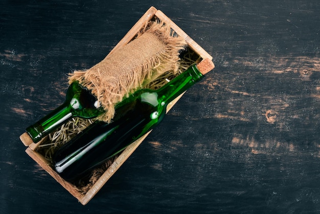 A bottle of old red wine in a box. On a black wooden background. Top view. Copy space for your text.