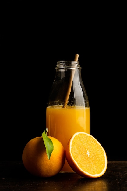 A bottle of orange juice and a halved orange on a dark background