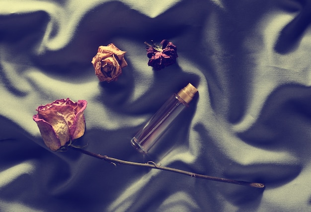 Photo a bottle of perfume and buds of dried roses on a gray silk.