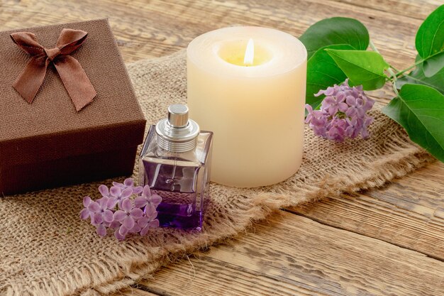 Bottle of perfume candle and lilac flowers on wooden background