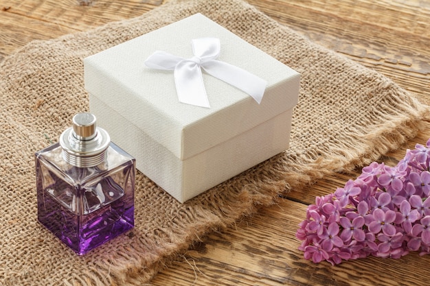 Bottle of perfume, a gift box and lilac flowers on sackcloth and old wooden boards. Concept of giving a gift on holidays. Top view.