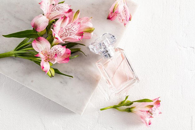 A bottle of perfume or toilet water with a floral light scent leaned on a marble white slab with pink flowers white background aroma presentation