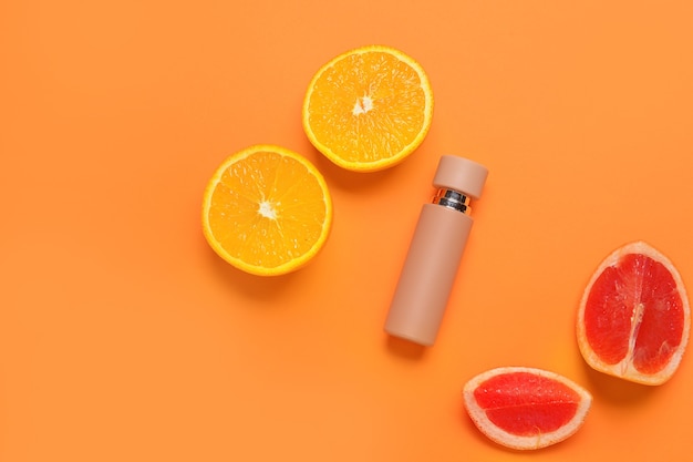 Bottle of perfume with citrus fruits on color