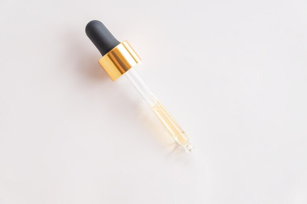 Bottle pipette dropper and Liquid yelloworange retinol or vitamin c gel or serum on a gray background