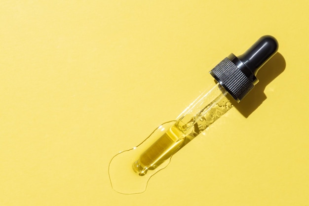 Flacone contagocce con retinolo liquido giallo o gel o siero di vitamina c su sfondo giallo striscio per la cura della pelle