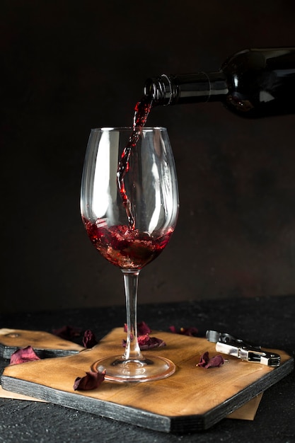 Bottle pouring red wine into glass on the black background