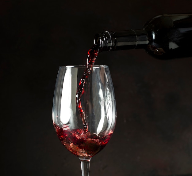 黒の背景のガラスに赤ワインを注ぐボトル