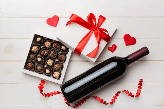 Bottle of red wine on colored background for Valentine Day with gift and chocolate Heart shaped with gift box of chocolates top view with copy space