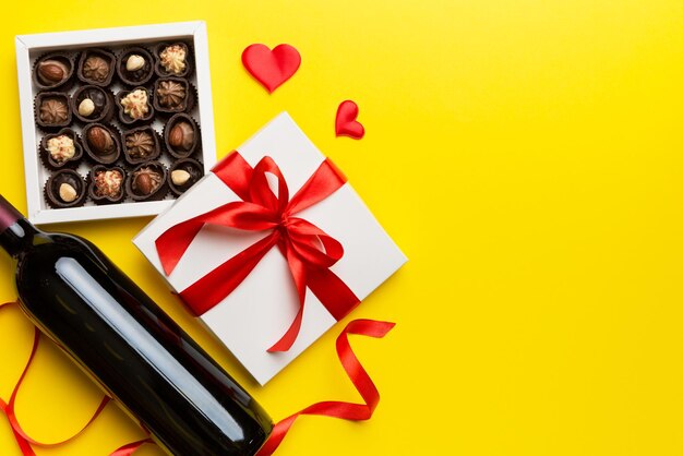 Bottle of red wine on colored background for valentine day with gift and chocolate heart shaped with gift box of chocolates top view with copy space