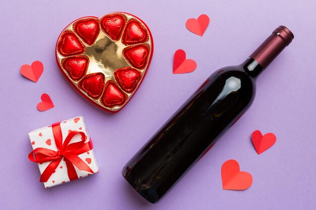 Bottle of red wine on colored background for valentine day with gift and chocolate heart shaped with gift box of chocolates top view with copy space