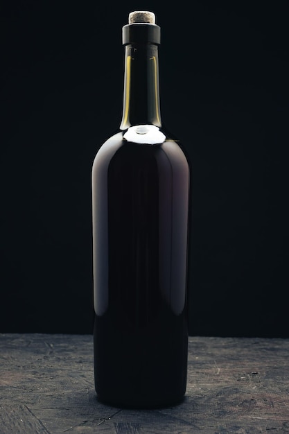 Bottle of red wine on a dark wooden table black background behaid