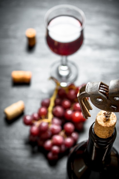 Bottle of red wine with a corkscrew. On a black wooden background.