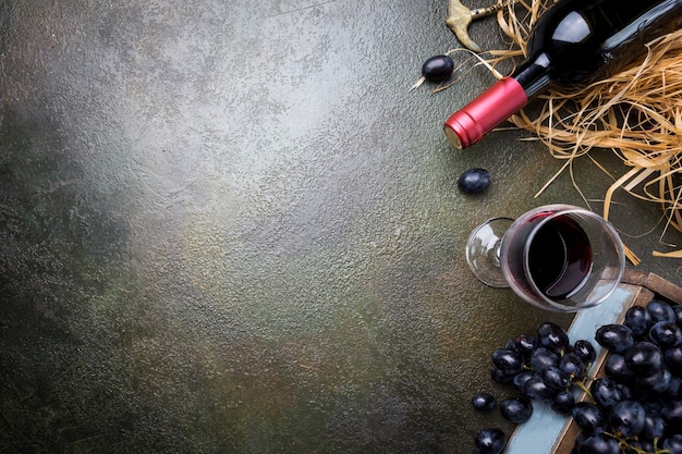 Una bottiglia di vino rosso con bicchiere e uva su pietra scura