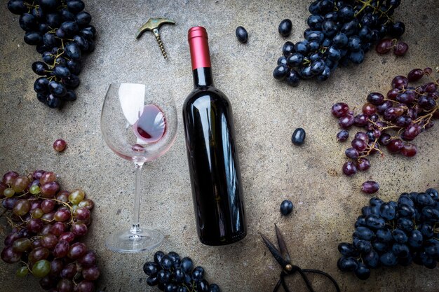 A bottle of red wine with glass and grapes on a gray stone