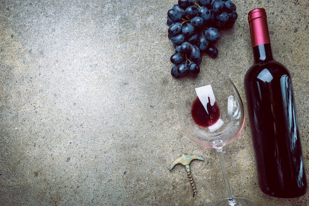 a bottle of red wine with glass and grapes on a gray stone