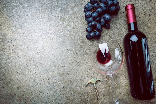 A bottle of red wine with glass and grapes on a gray stone