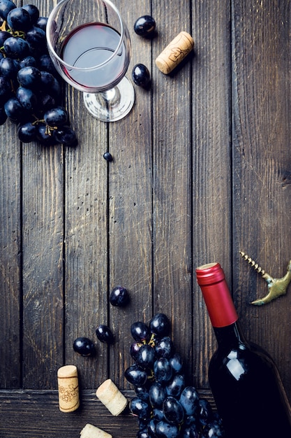 A bottle of red wine with glass and grapes over wooden