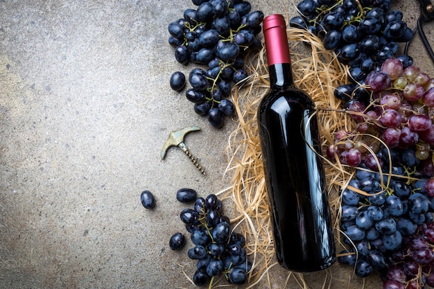 A bottle of red wine with grapes on a gray stone