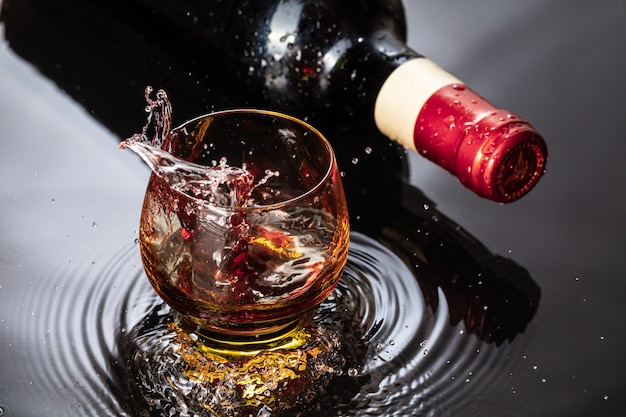 Bottle of red wine with wineglass. Water splash and droplet on the black reflection.